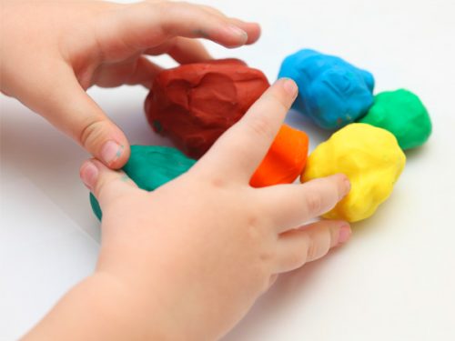 Mãos de uma criança a tocar em várias bolas de plasticina