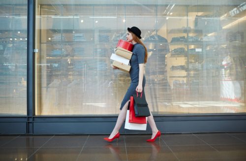 Mulher com sacos e e caixas de compras em frente a uma montra