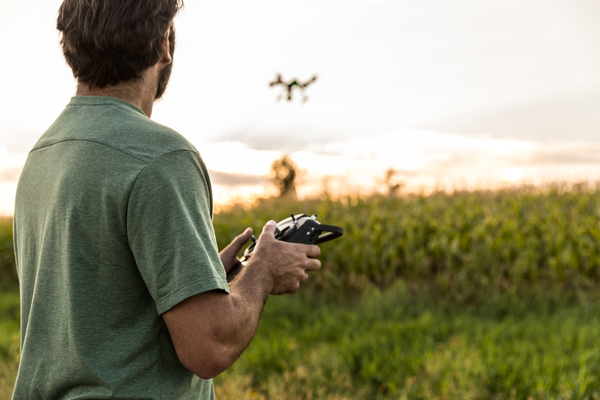 Homem a comandar um drone numa zona agrícola